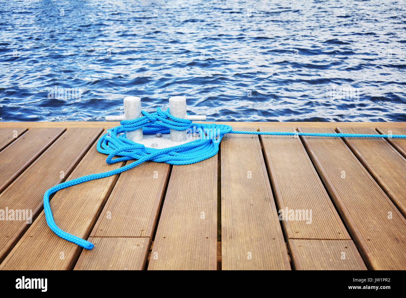 Cleat with blue rope on a wooden pier, safe journey concept. Stock Photo