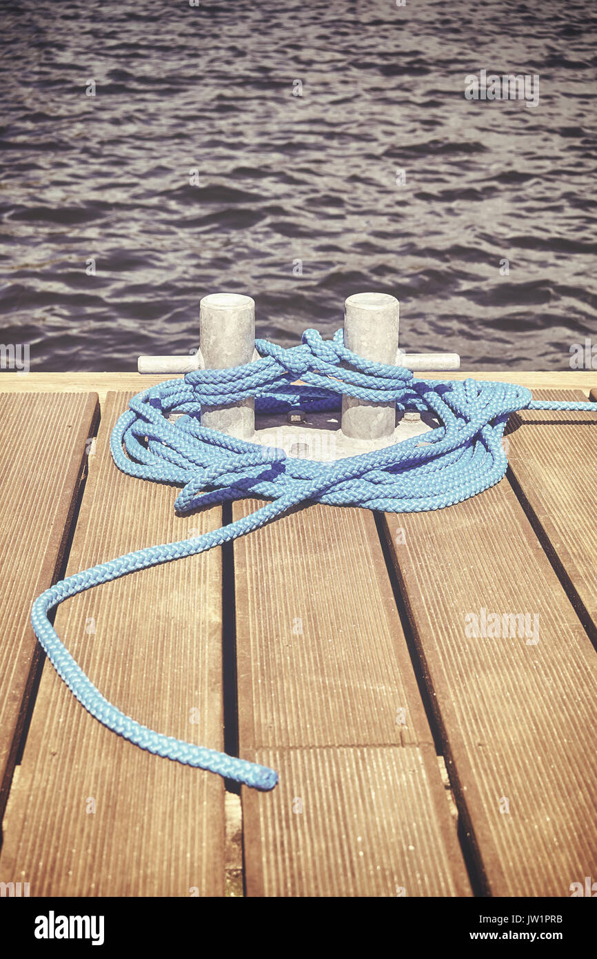 Retro toned picture of a cleat with blue rope on a wooden pier, safe travel concept. Stock Photo