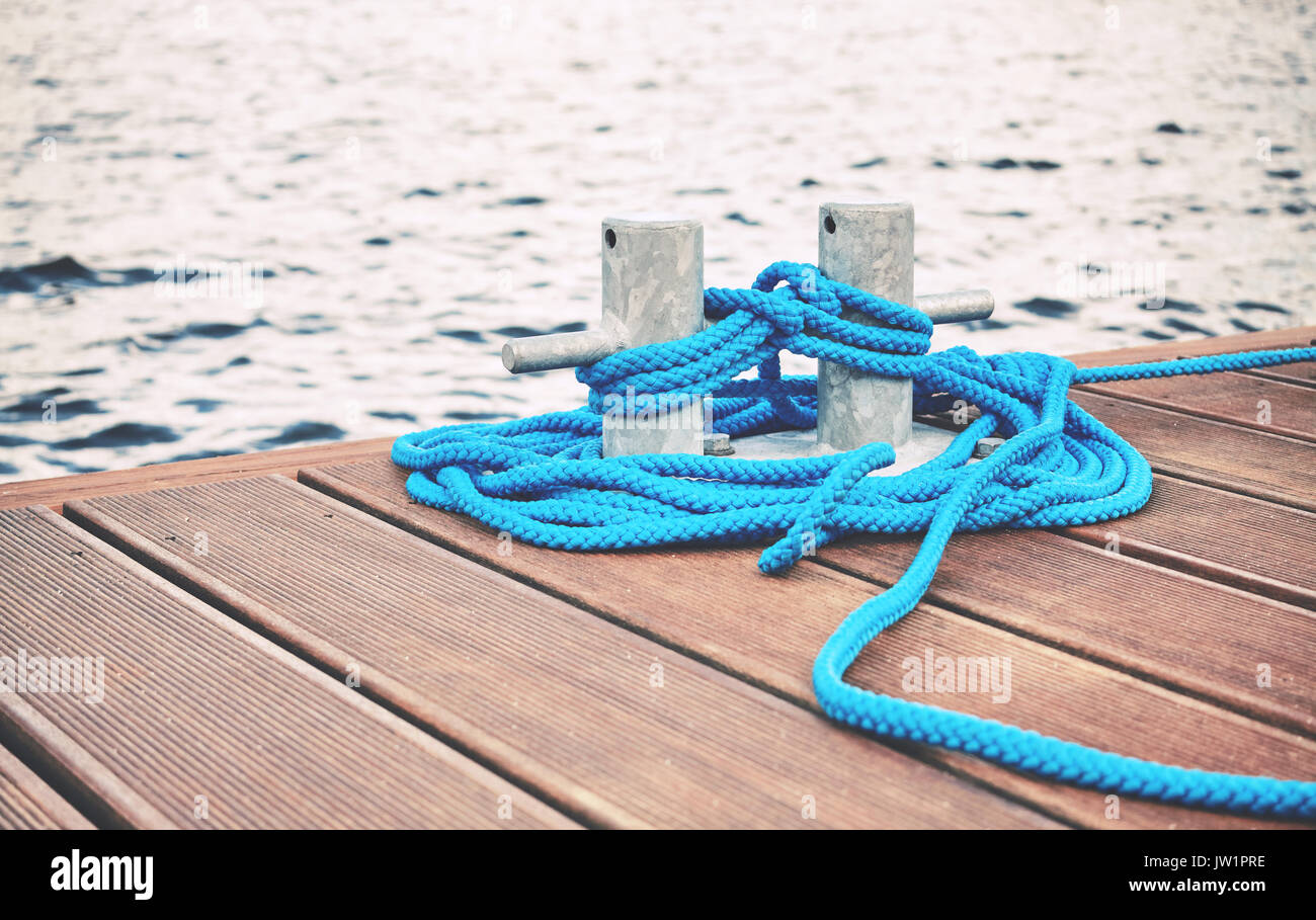 Cleat with blue rope on a wooden pier, travel or safety concept, color toning applied. Stock Photo