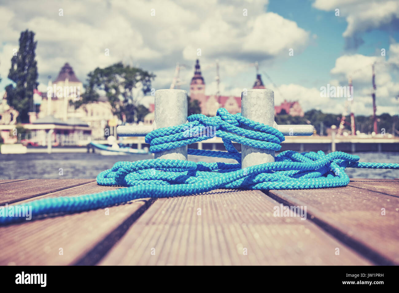 Cleat with blue rope on a wooden pier, Szczecin waterfront in distance, Poland. Stock Photo