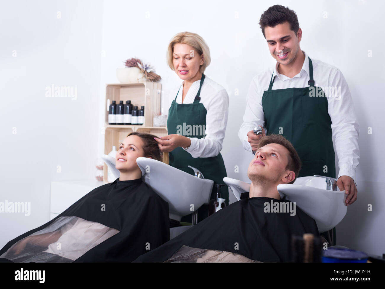 Two hairdressers working with hair of clients in washing tray