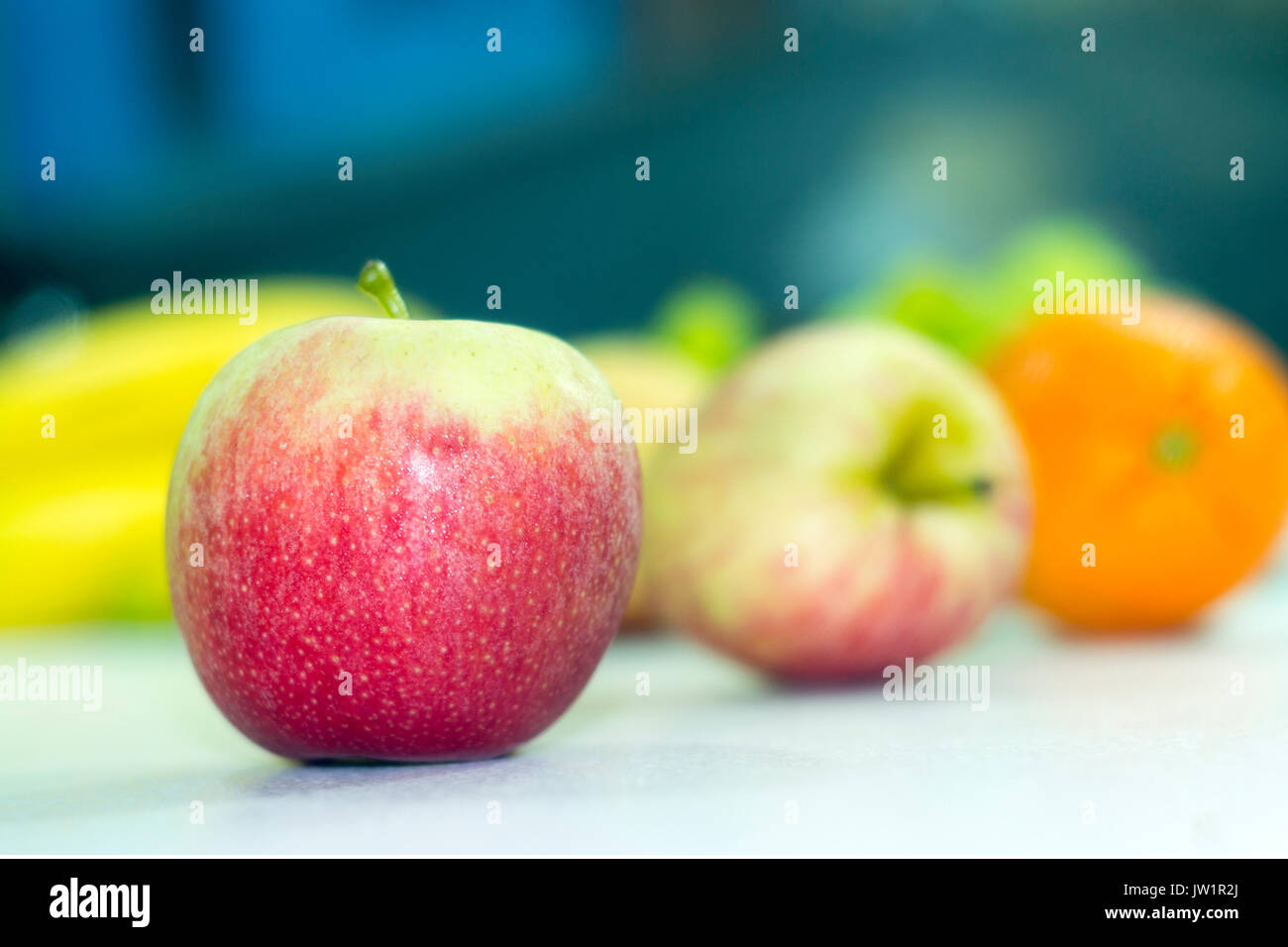 Manzana roja en meza con otras frutas desenfocadas, alimento saludable y natural con vitaminas, baja en calorías, apetecible y jugosa, de clima frío Stock Photo