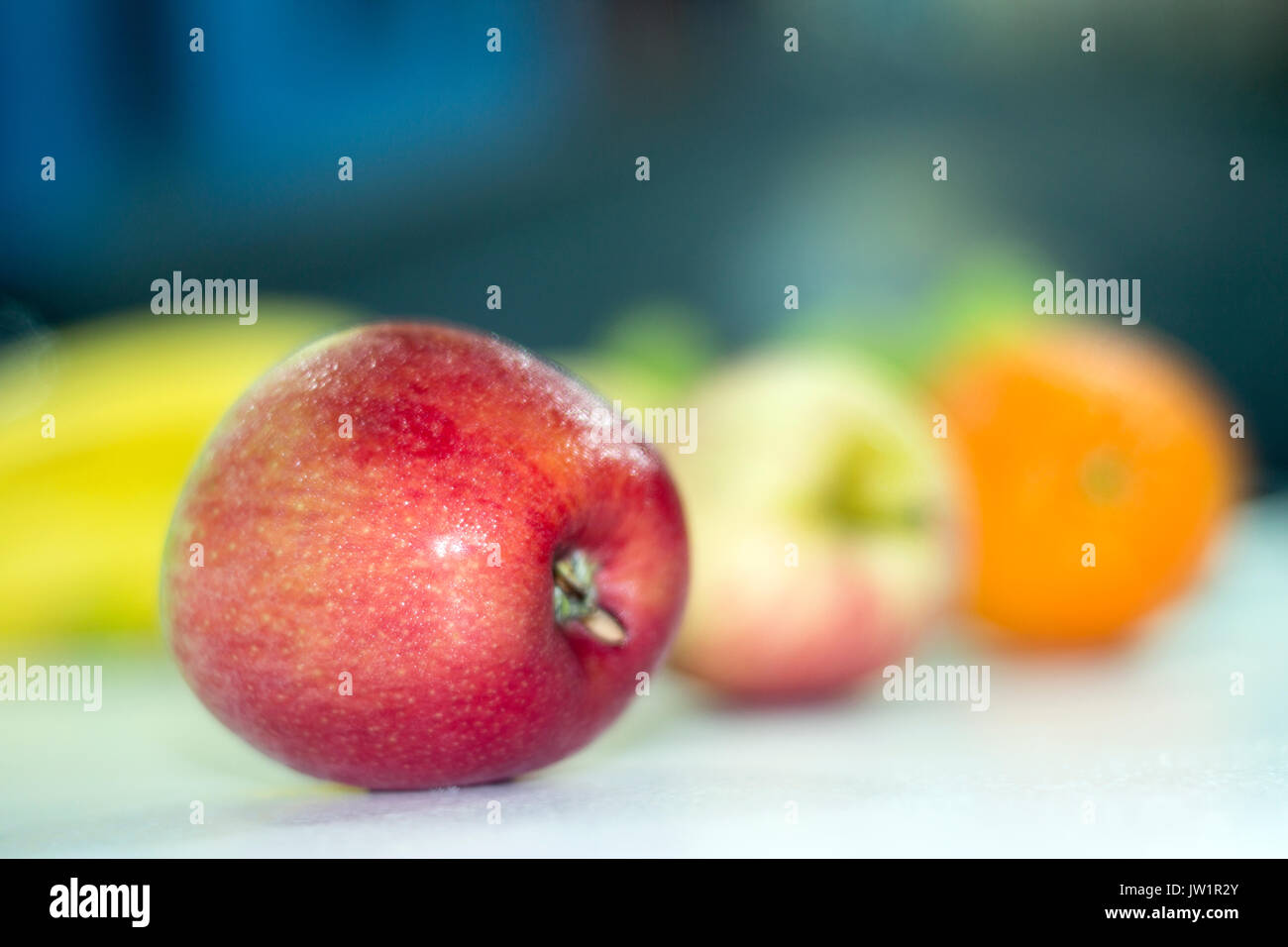 Manzana roja en meza con otras frutas desenfocadas, alimento saludable y natural con vitaminas, baja en calorías, apetecible y jugosa, de clima frío Stock Photo