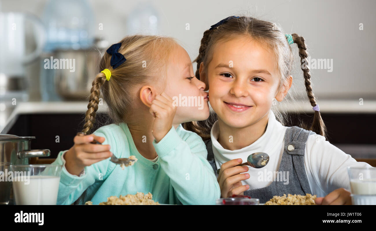 Portrait of smiling cute little sisters eating porridge in kitchen Stock Photo