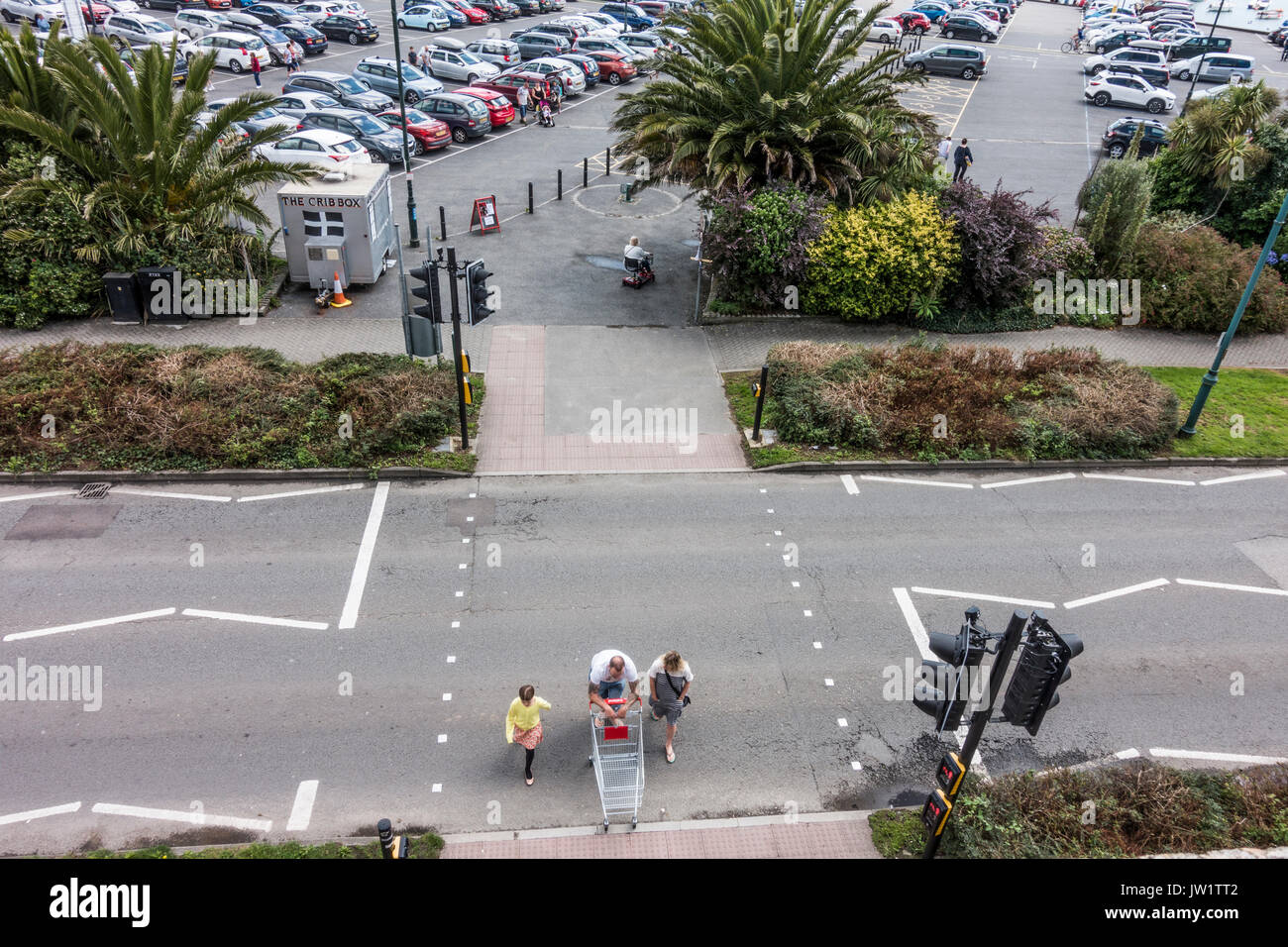Family crossing the road at the lights from the car park, with dad pushing a shopping trolley to the facilities of Penzance, Cornwall, England, UK. Stock Photo