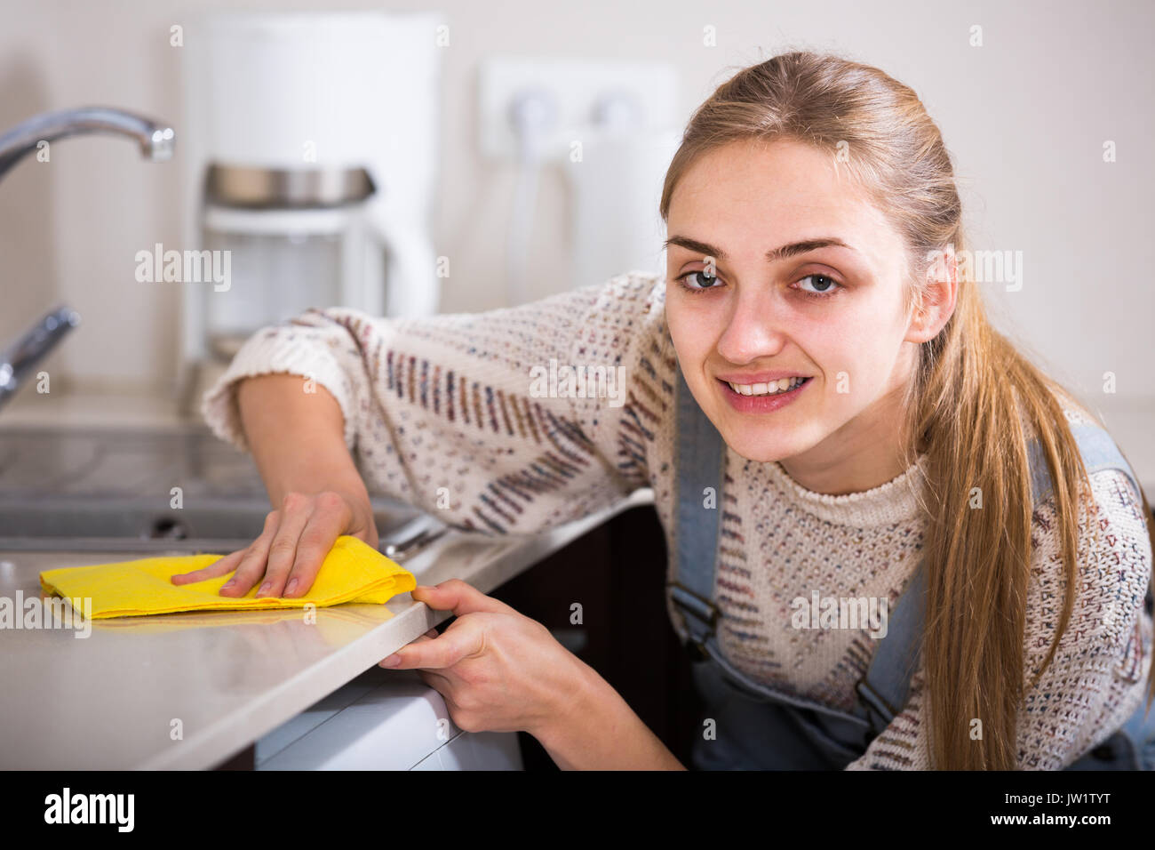 Cheerful adult spanish girl dusting surfaces in residential kitchen
