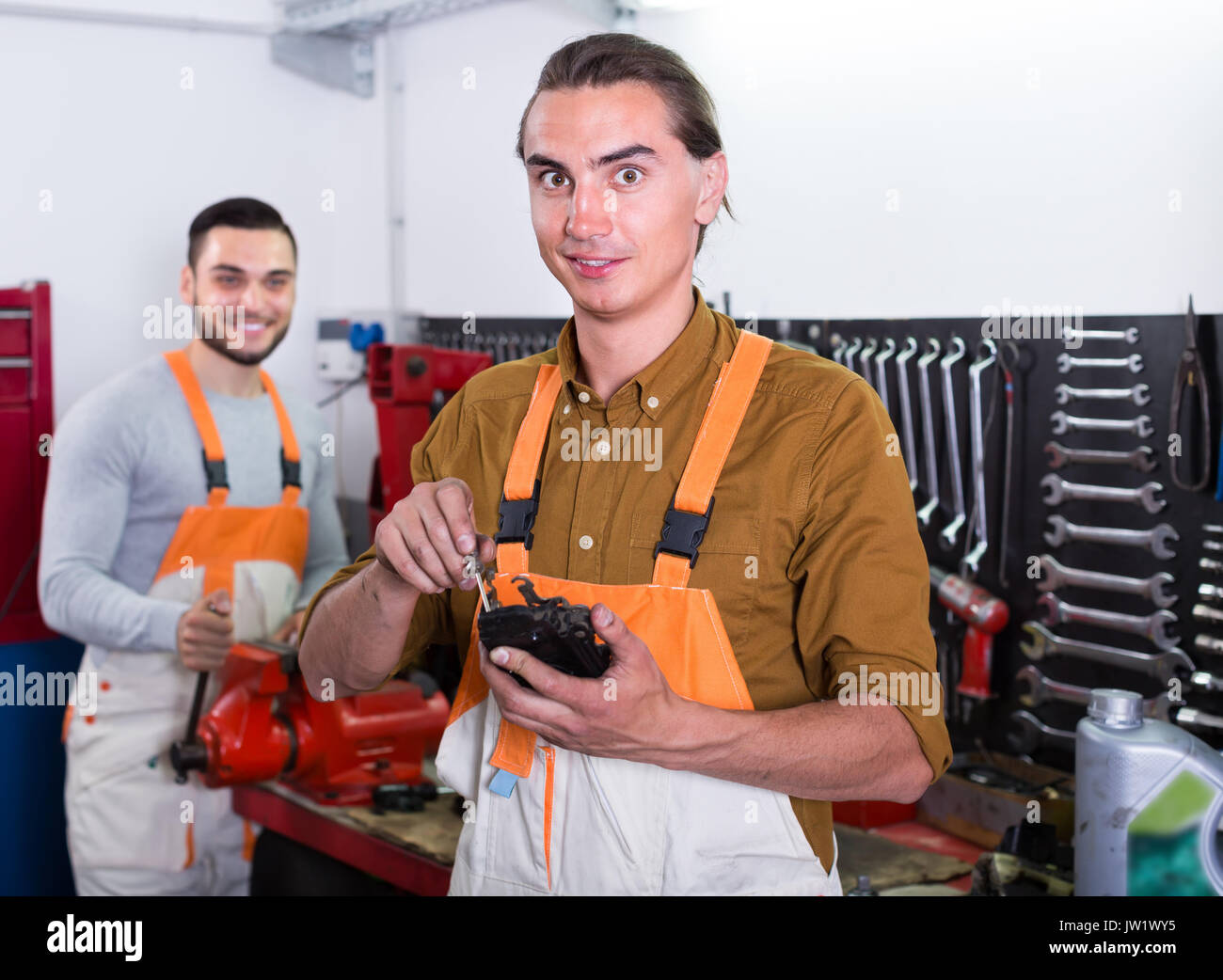 Two cheerful positive mechanics toiling in locksmiths workshop and smiling Stock Photo
