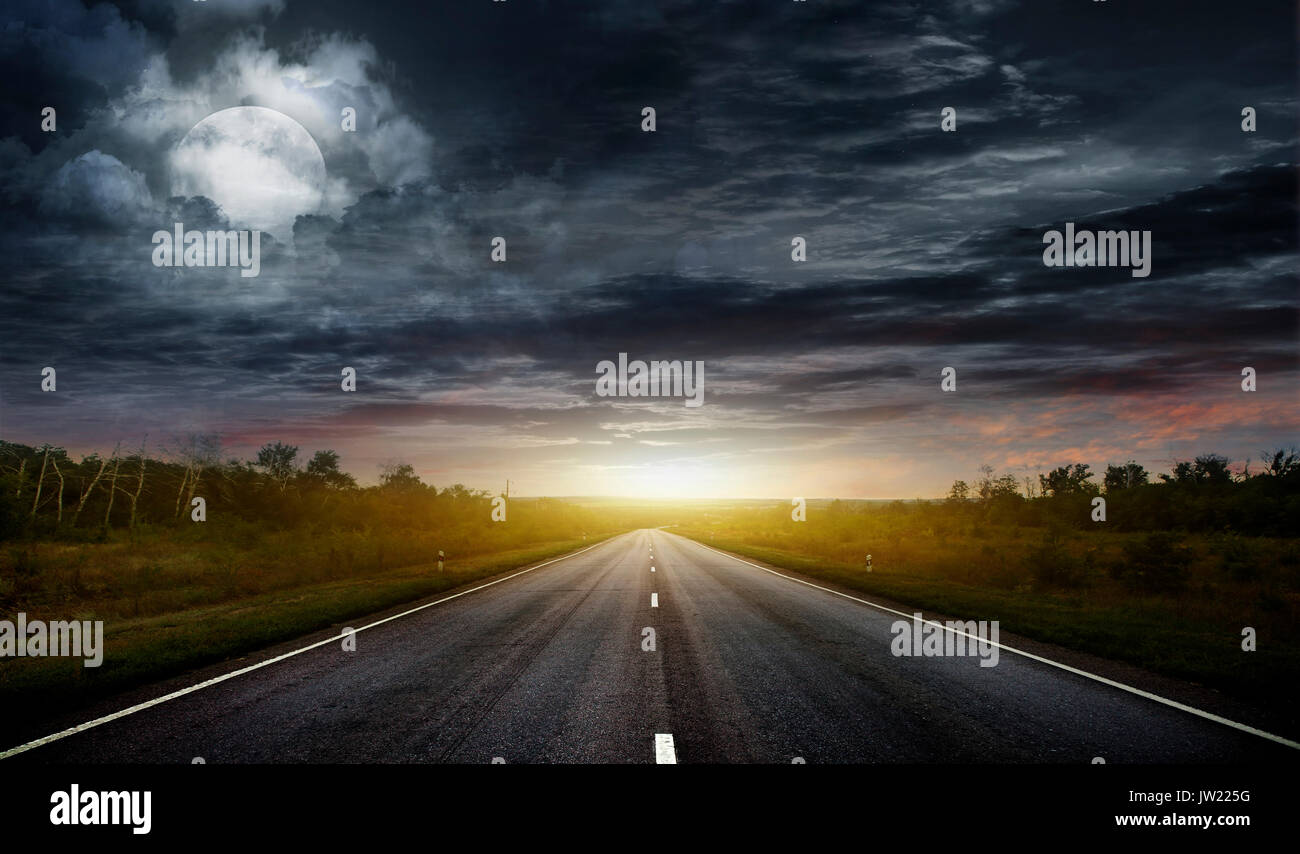 Long country road with white lines down the centre stretching off past a lone tree to the distant horizon Stock Photo