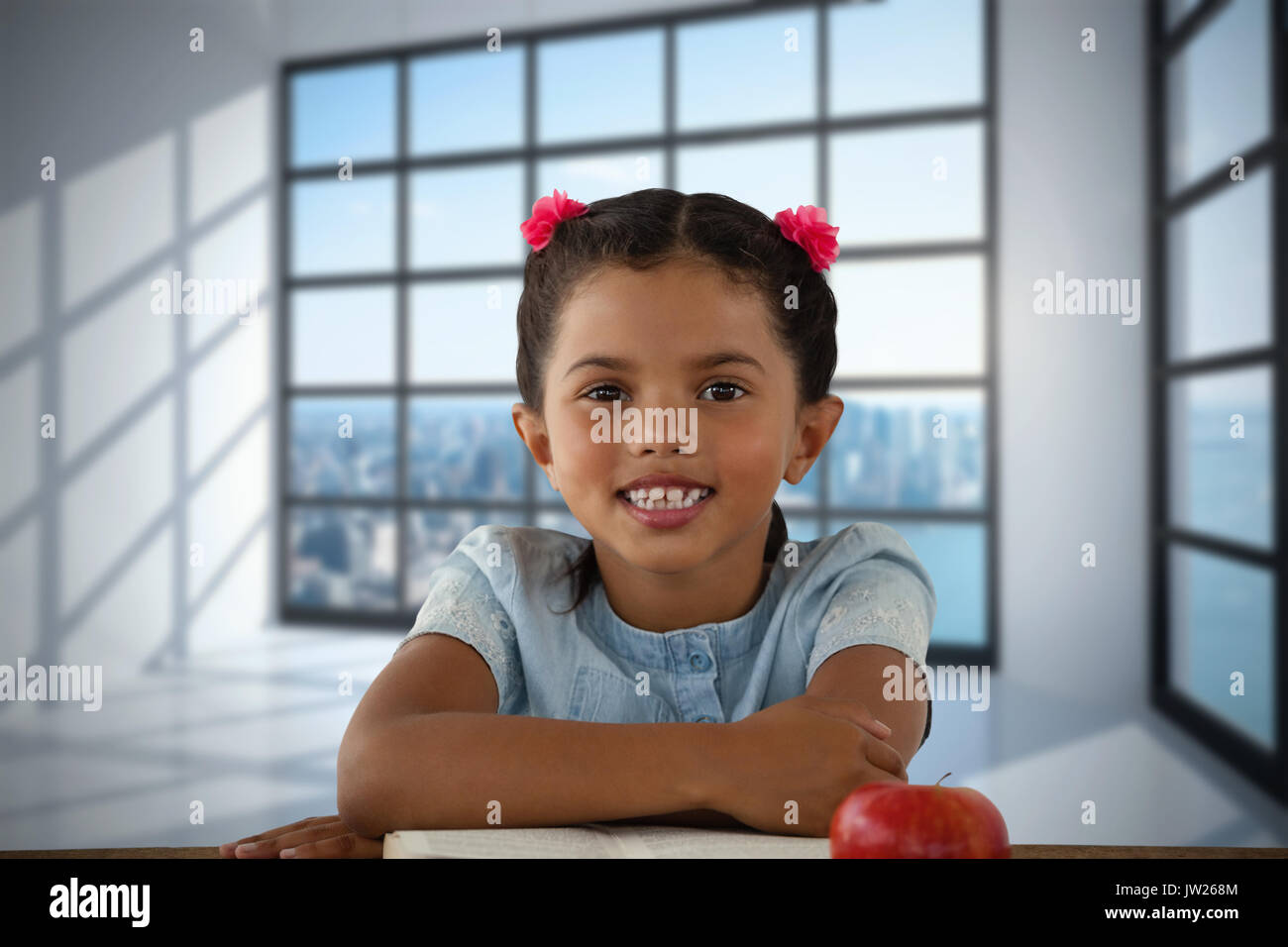 Smiling girl sitting at desk against room with large window showing city Stock Photo