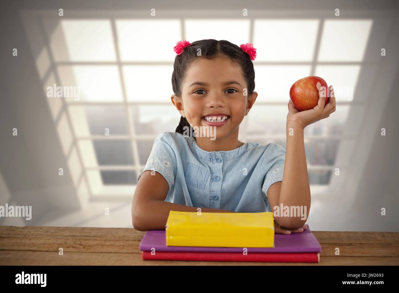 Smiling girl holding apple against room with large window showing city Stock Photo