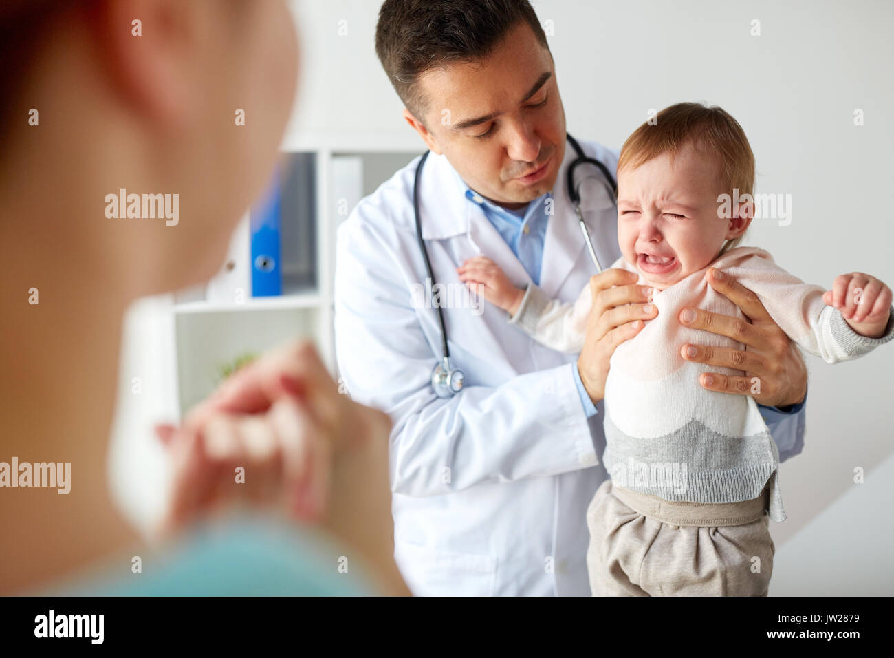 doctor or pediatrician with crying baby at clinic Stock Photo