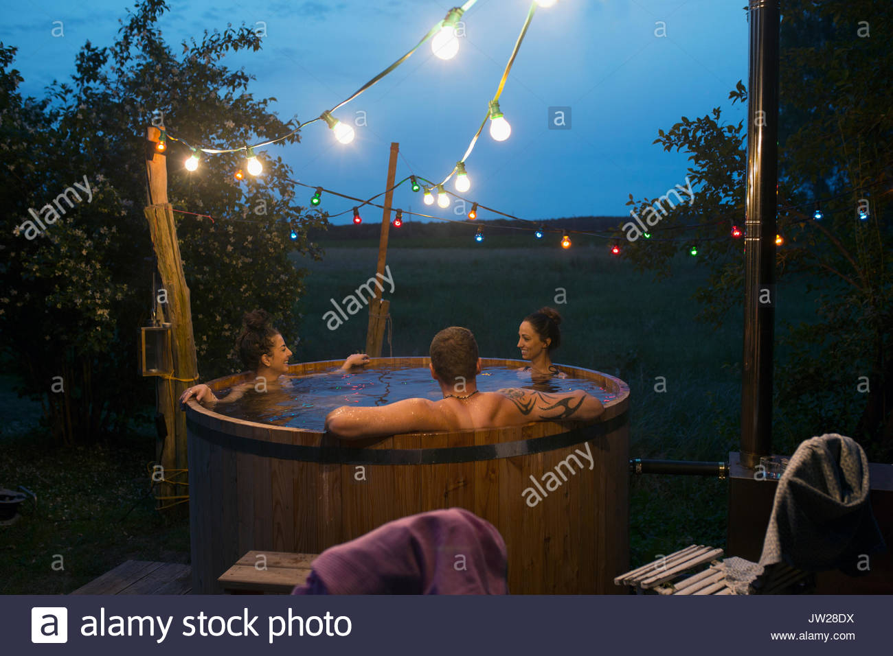 Friends relaxing, soaking in hot tub under string lights on night Stock