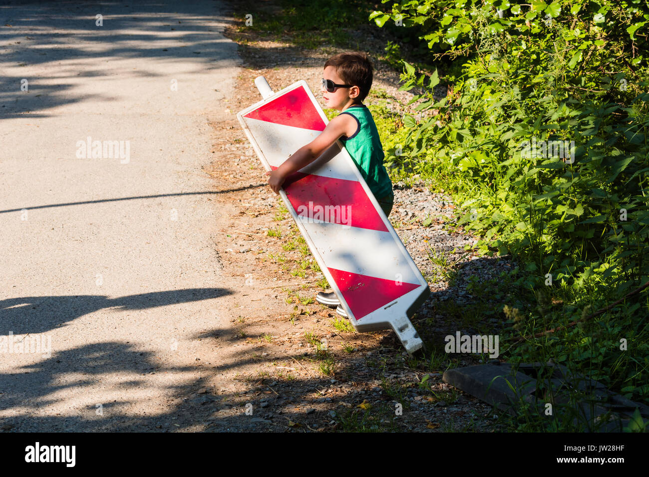 Little boy is carrying a construction site barrier across the street. To overcome difficulties Stock Photo