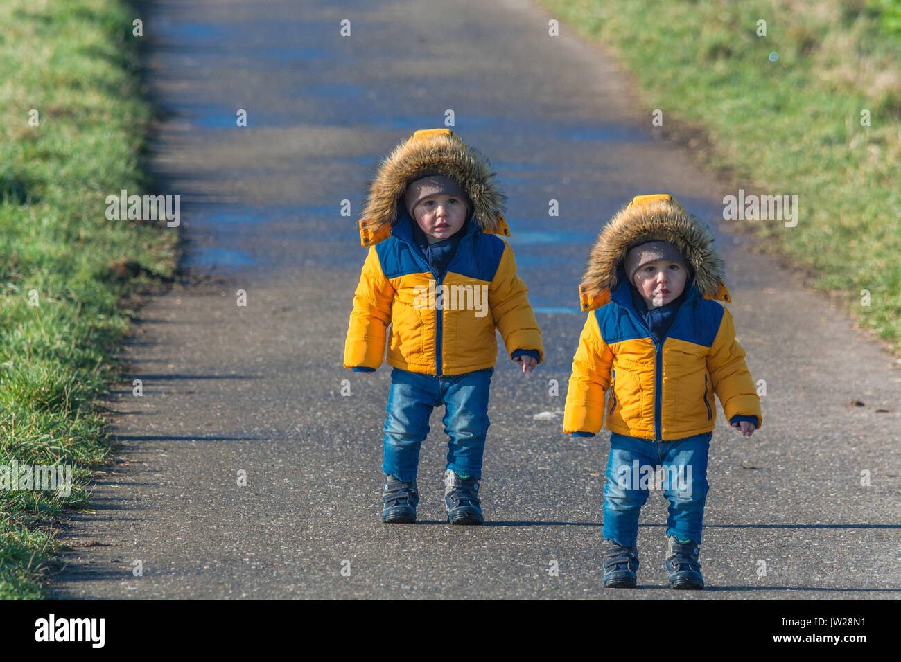 Two small children, twins walking on a country road and looking amazed at the camera. Stock Photo