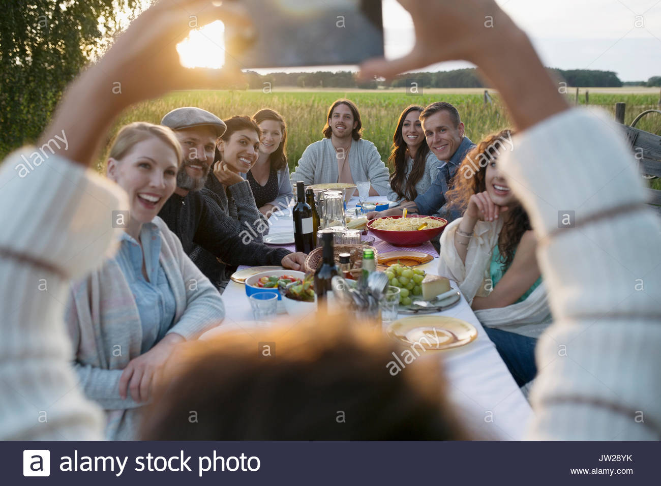 Woman with camera phone photographing friends enjoying garden dinner party in rural yard Stock Photo