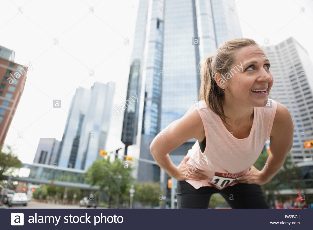 Female runner resting with hands on hips on urban street Stock Photo