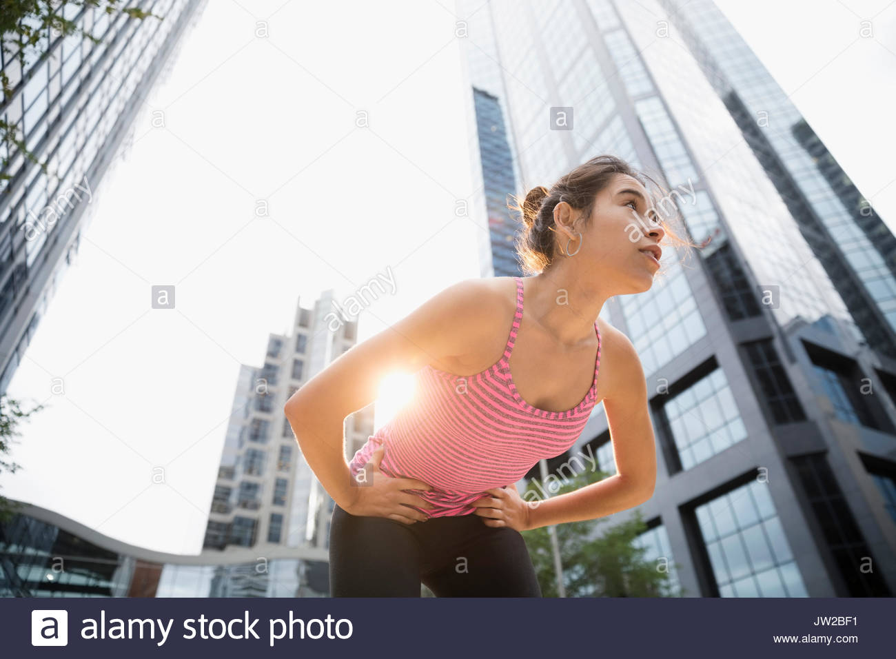 Tired young female runner resting, bending below urban highrise building Stock Photo