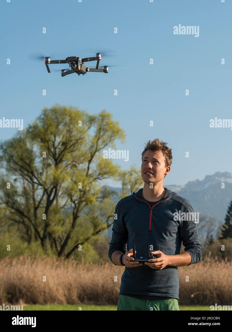 Young man controlling flying quadrocopter, remote controlled drone with camera, DJI Mavic Stock Photo