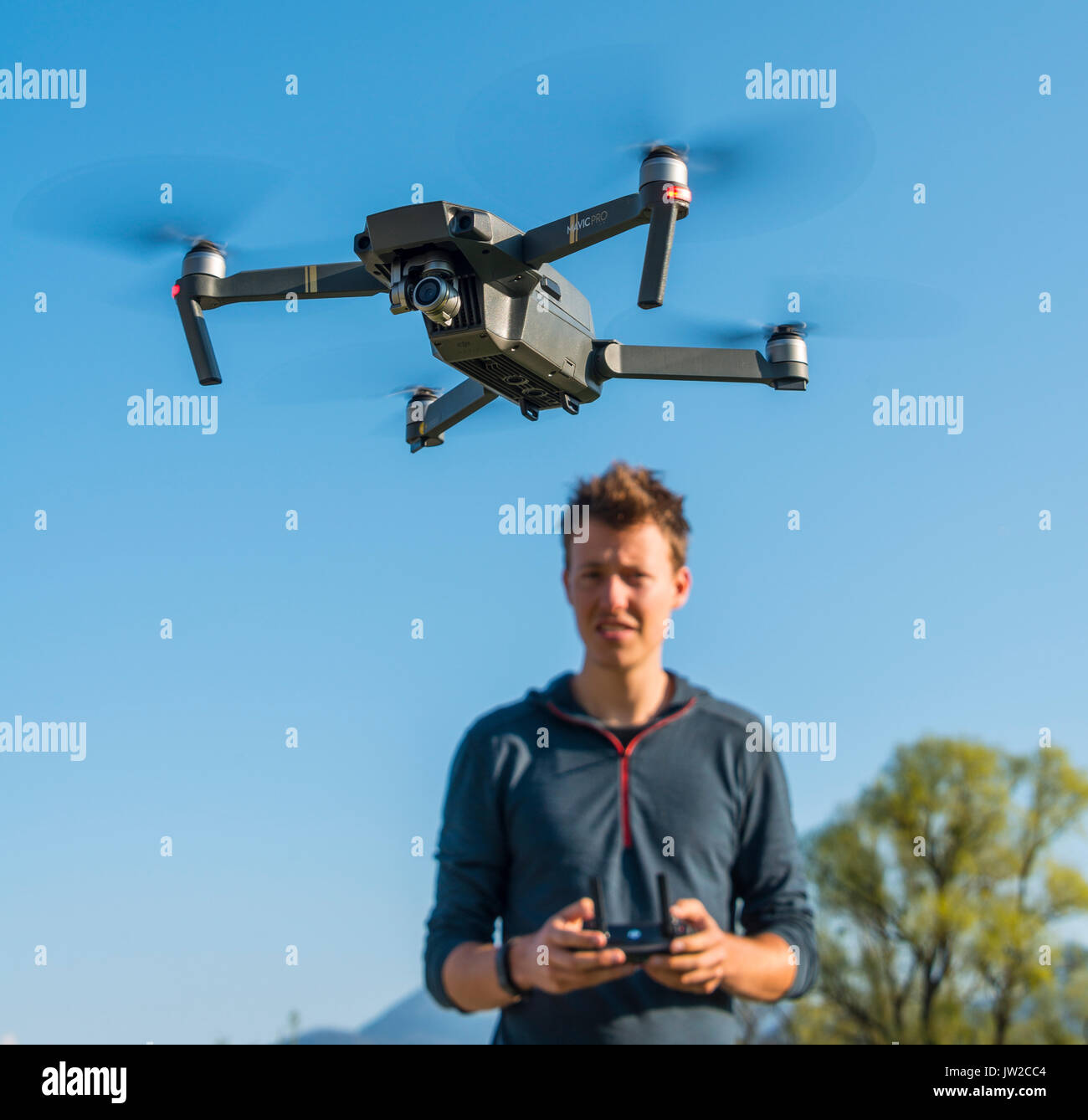 Young man controlling flying quadrocopter, remote controlled drone with camera, DJI Mavic Stock Photo