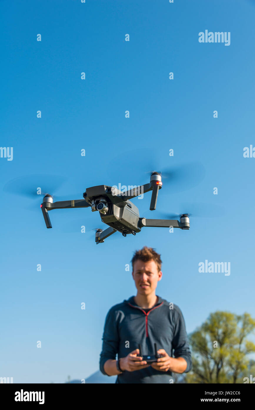 Young man controlling flying quadrocopter, remote controlled drone with camera, DJI Mavic Stock Photo
