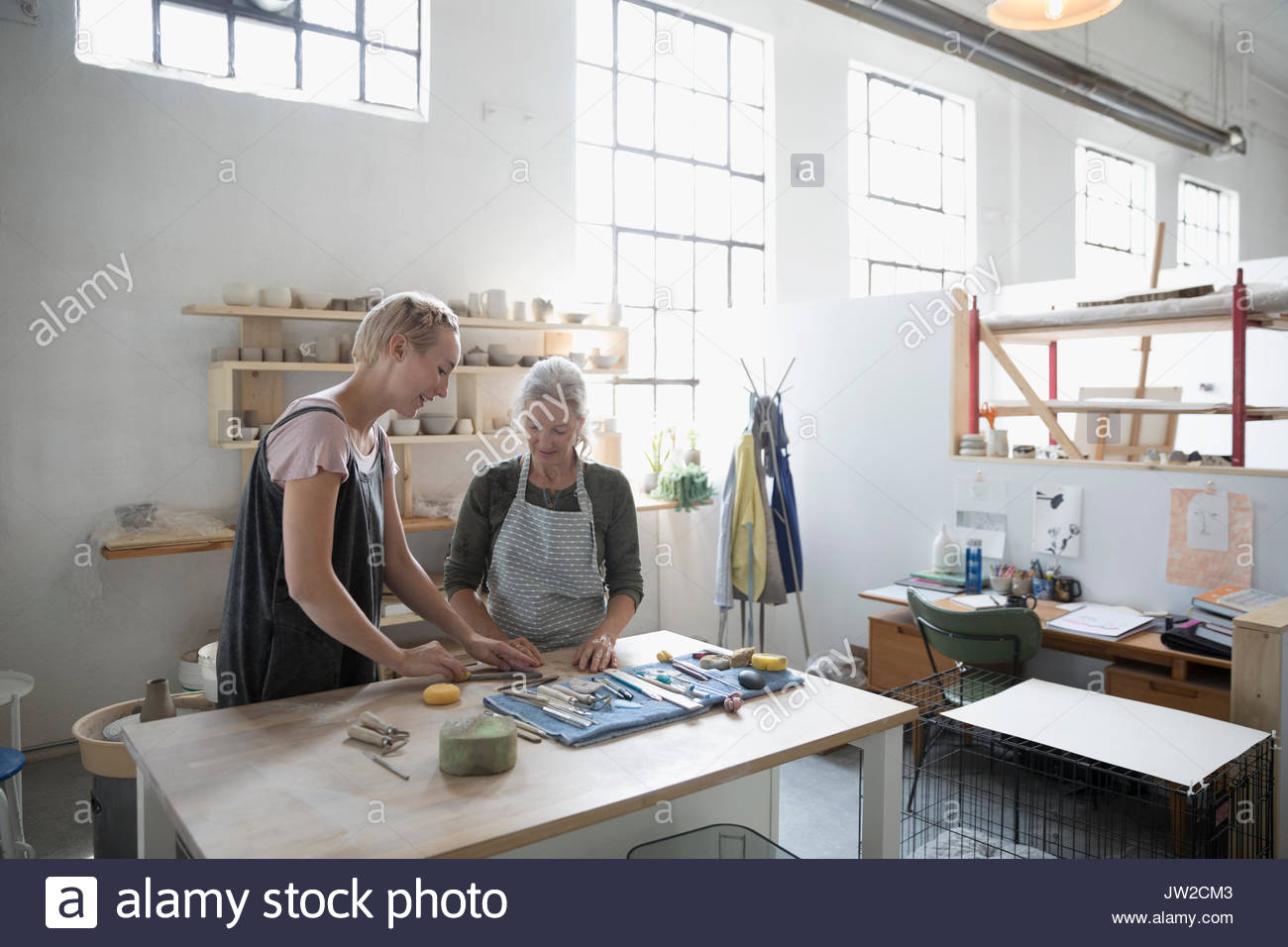 Female instructor helping pottery student preparing clay at workbench