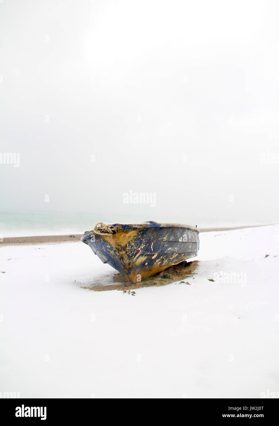Old abandoned blue wooden boat under white snow on beach, lake covered by snow and foot traces, panoramic view of winter landscape in the beach Stock Photo