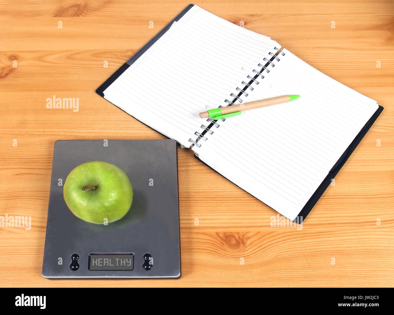 Open blank pages notebook with green apple on kitchen scale representing health diet lifestyle concept Stock Photo