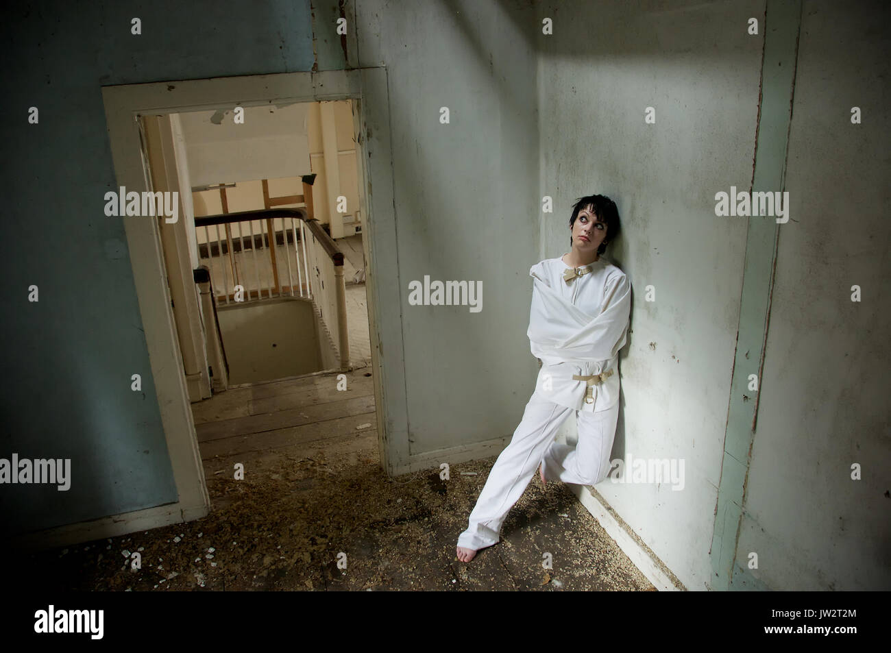 dark haired girl in a straight-jacket in an abandoned house Stock Photo