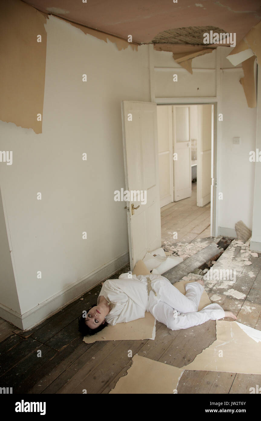 dark haired girl in a straight-jacket in an abandoned house Stock Photo