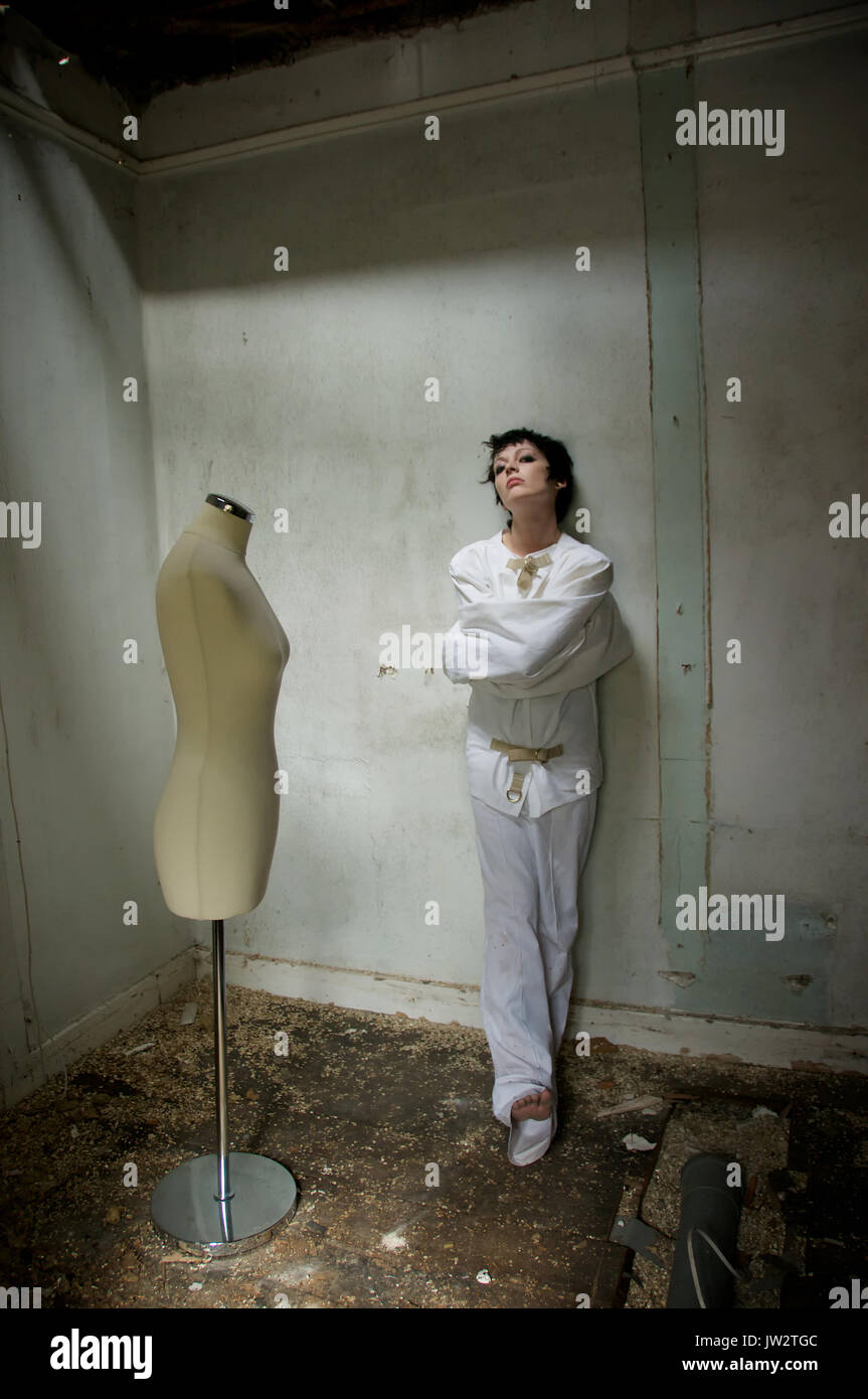 dark haired girl in a straight-jacket in an abandoned house Stock Photo