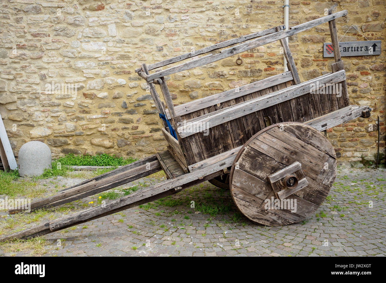 Old wooden cart with a stone masonry wall on the background with a 'cartiera' sign (paper mill in Italian language). Stock Photo