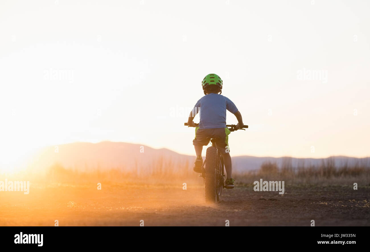 USA, Colorado, Rear view of boy (8-9) cycling at sunset Stock Photo