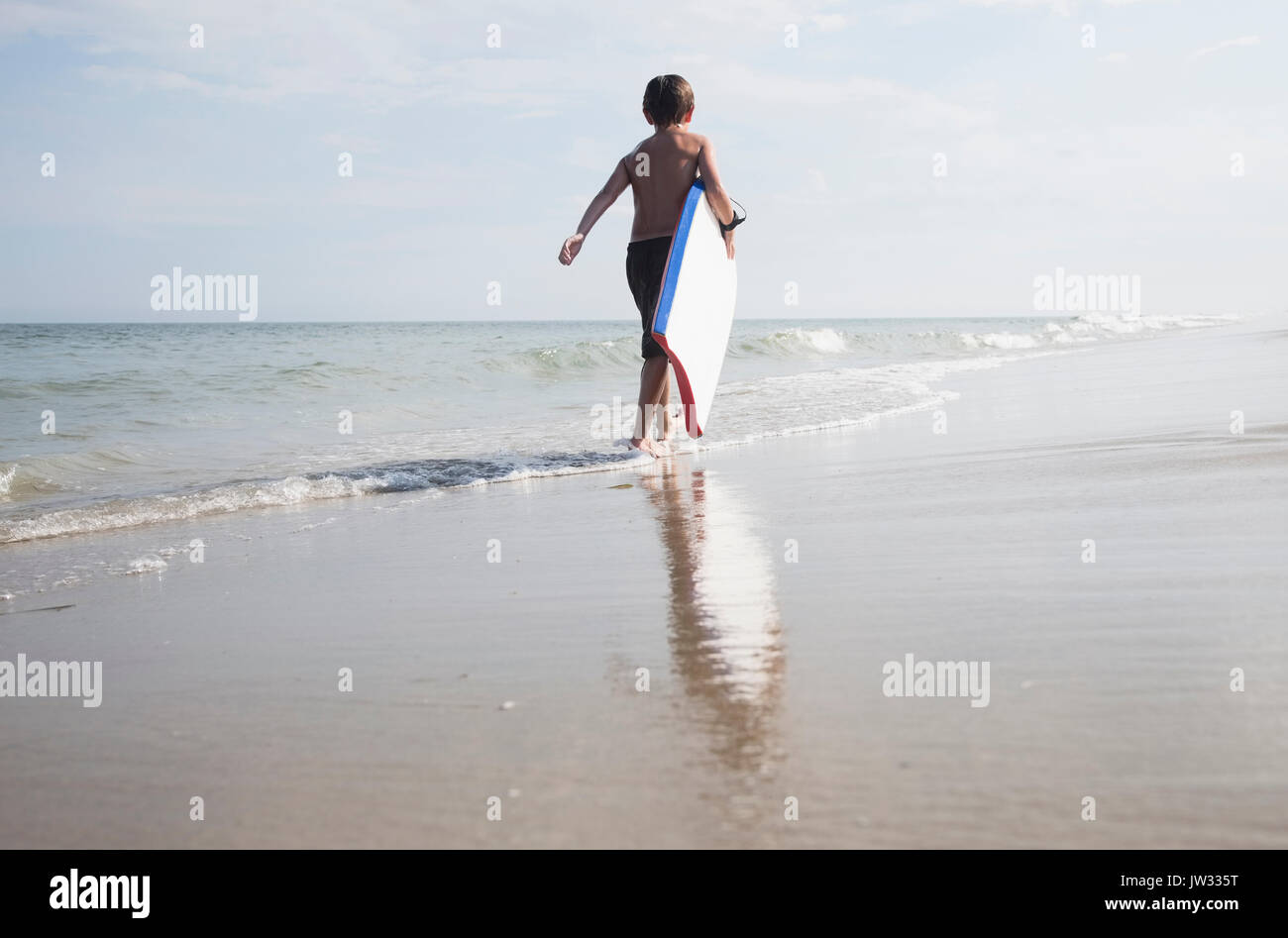 Boy (8-9) walking and carrying body board in empty beach Stock Photo