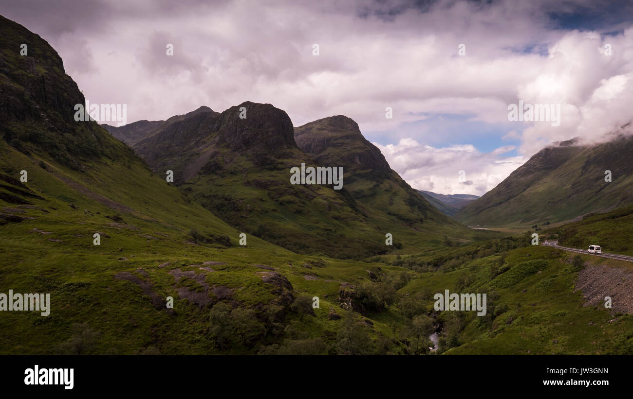 A small bus drives along the Three Sisters of Glencoe. The image shows the beautiful nature of the mountains and valley of Glencoe, Scotland. Stock Photo