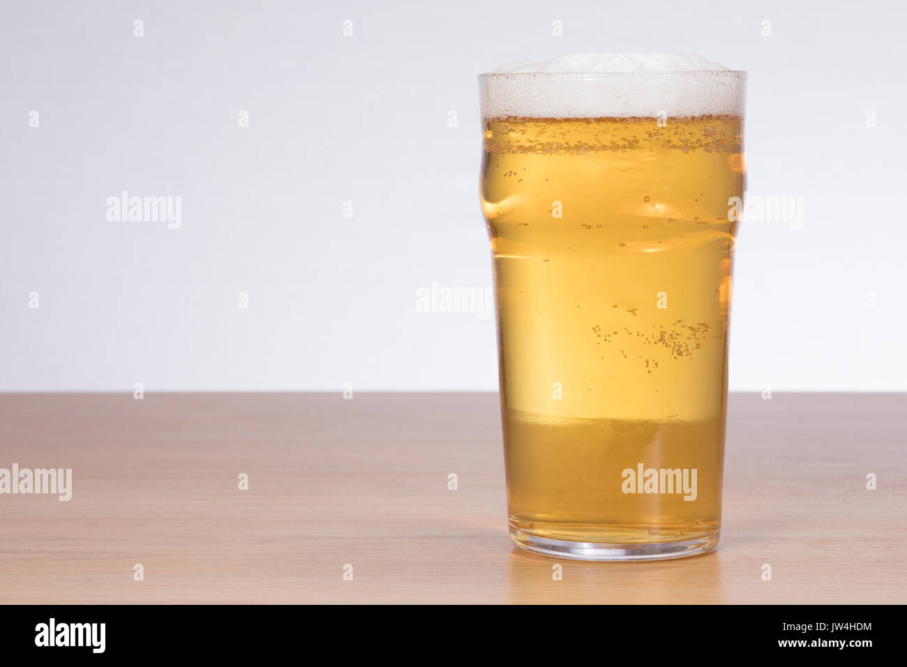 A freshly poured, crisp, frothy pint of beer on a timber table top with white background and copy space. Stock Photo