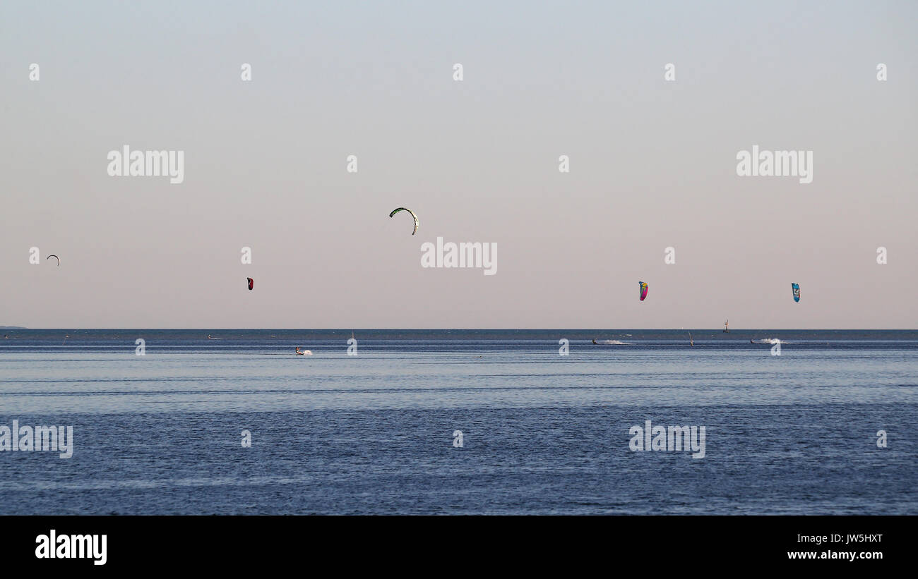 Kitesurfing off shore against a pink and blue hazy sky after sunset Stock Photo