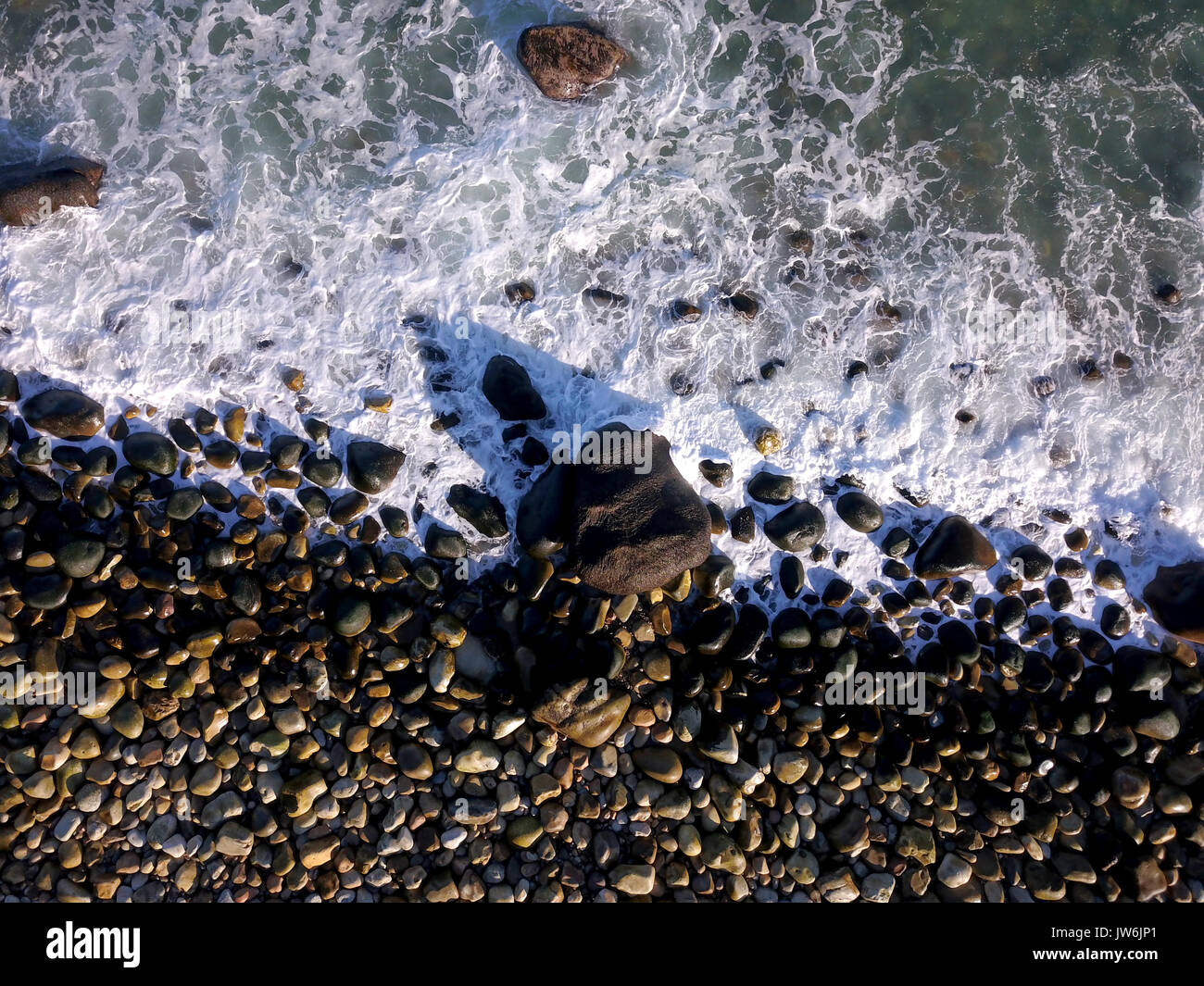 Aerial over waves crashing into a rocky beach Stock Photo