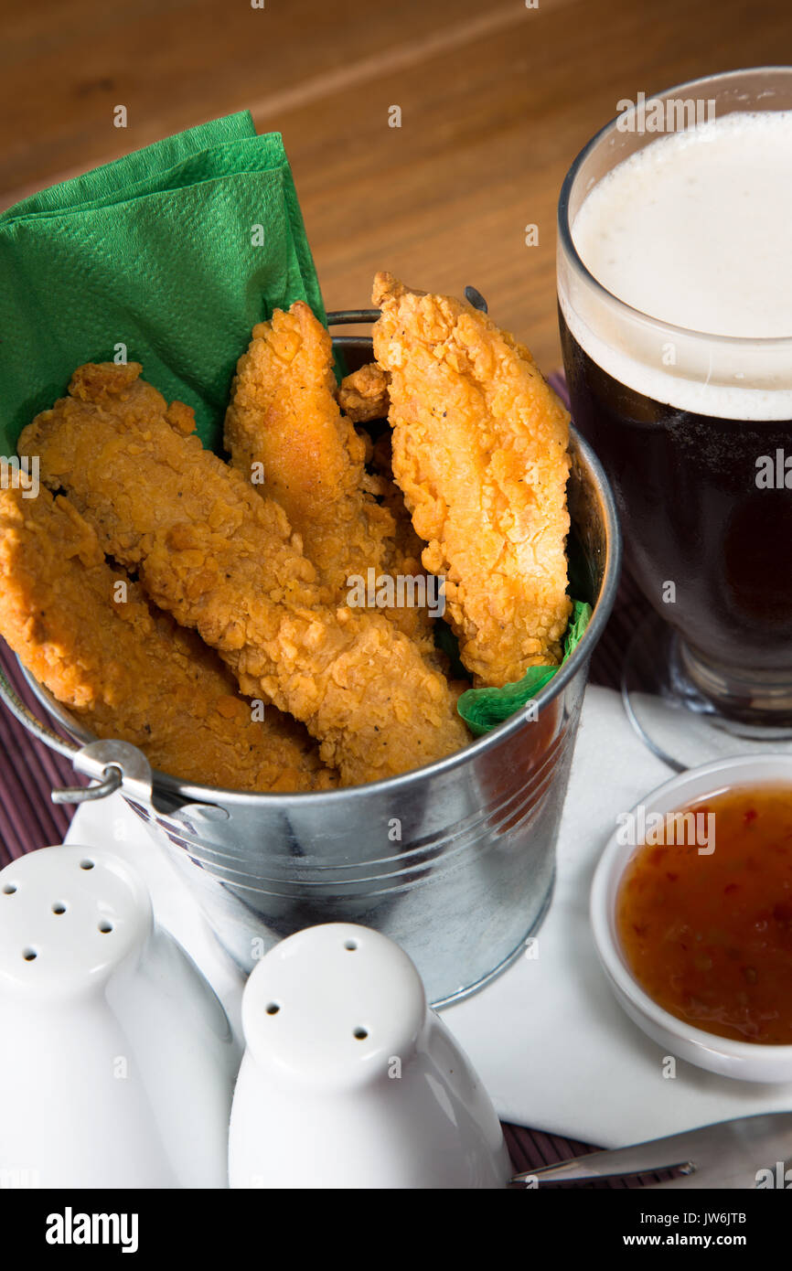 A pub/restaurant lunch/ snack of Hot and Spicy breaded Chicken fillets with a Sweet Chili dip and a glass of ale. Stock Photo
