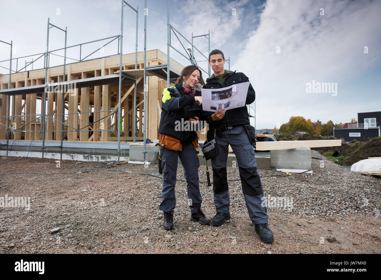 Full length of male and female carpenters discussing about plan against incomplete building Stock Photo