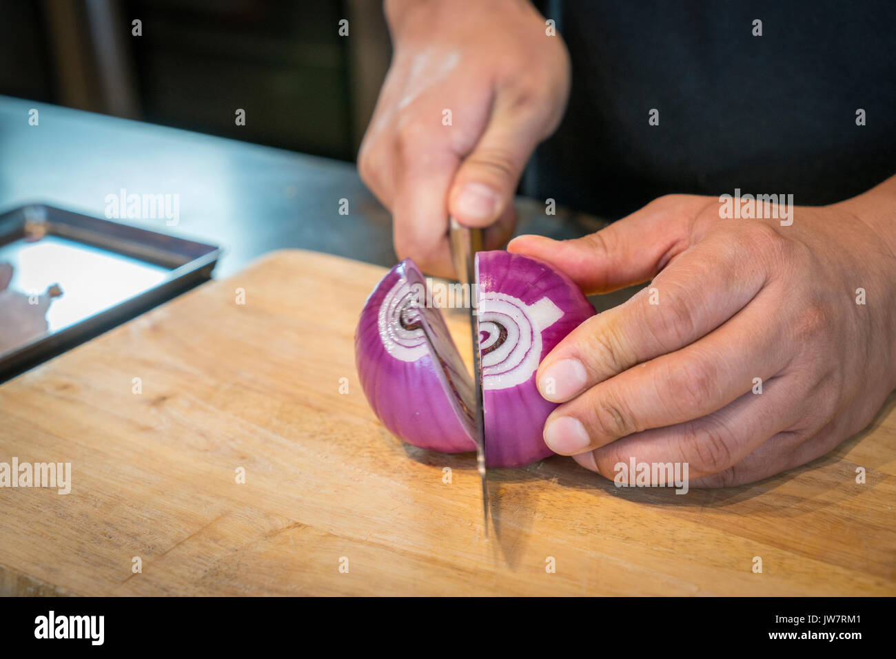 Chef chopping a red onion with a knife on the cutting board. Stock Photo