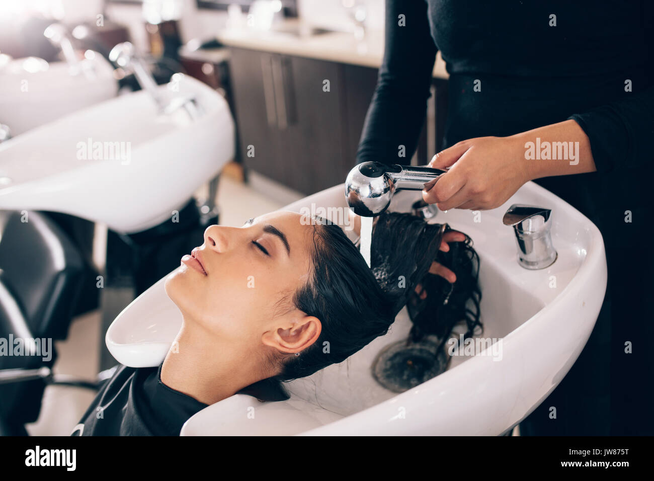 Closeup of female hairdresser rinsing hair of a customer . Woman getting hair spa at hair dressing salon. Stock Photo