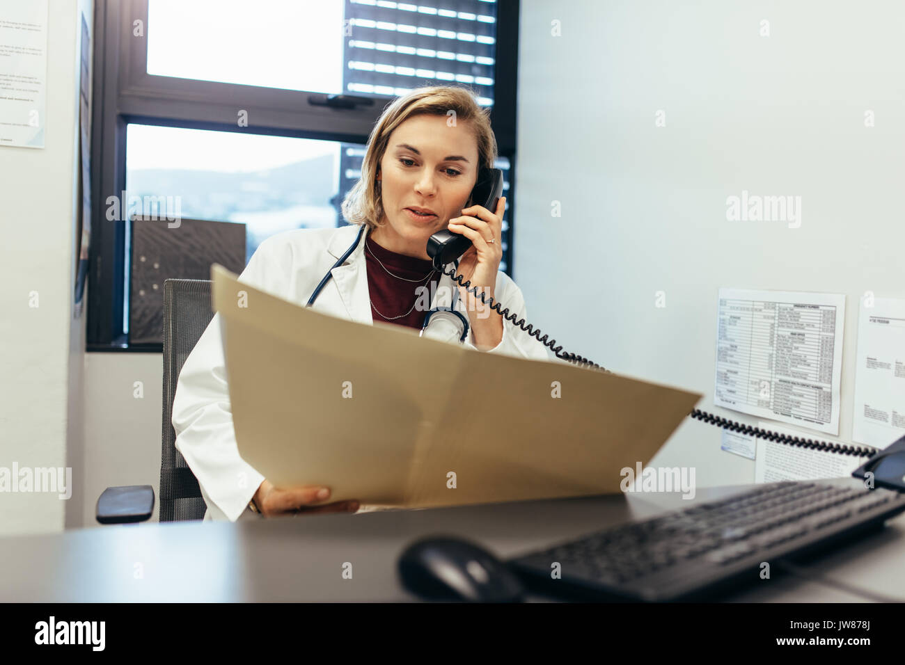 Doctor reading medical records and talking on telephone.  Medicine practitioner examining medical reports and using telephone in her clinic. Stock Photo