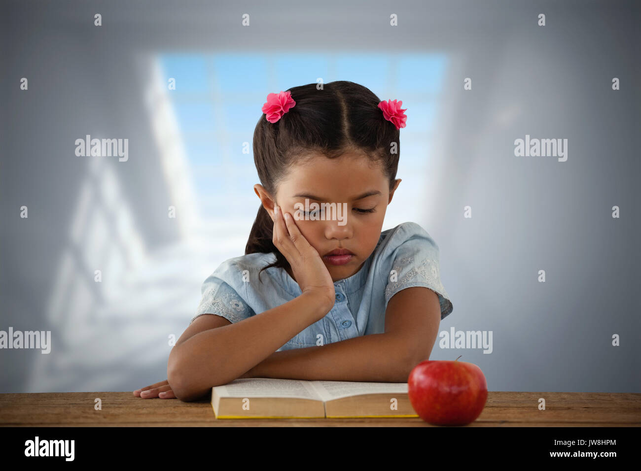 Concentrated girl reading book at desk against room with large windows Stock Photo