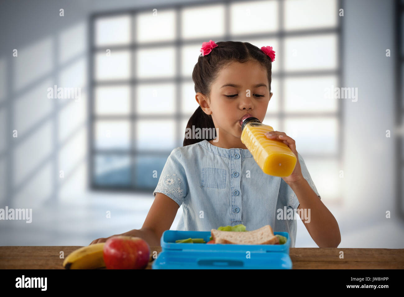 Girl drinking juice at table against room with large windows showing city Stock Photo