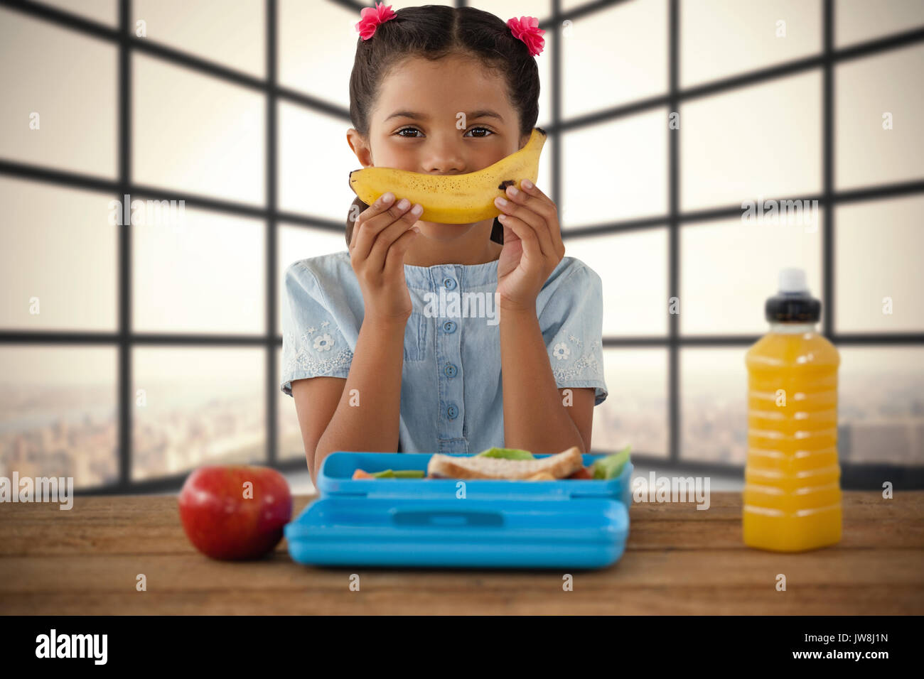 Girl holding banana at table against room with large window showing city Stock Photo