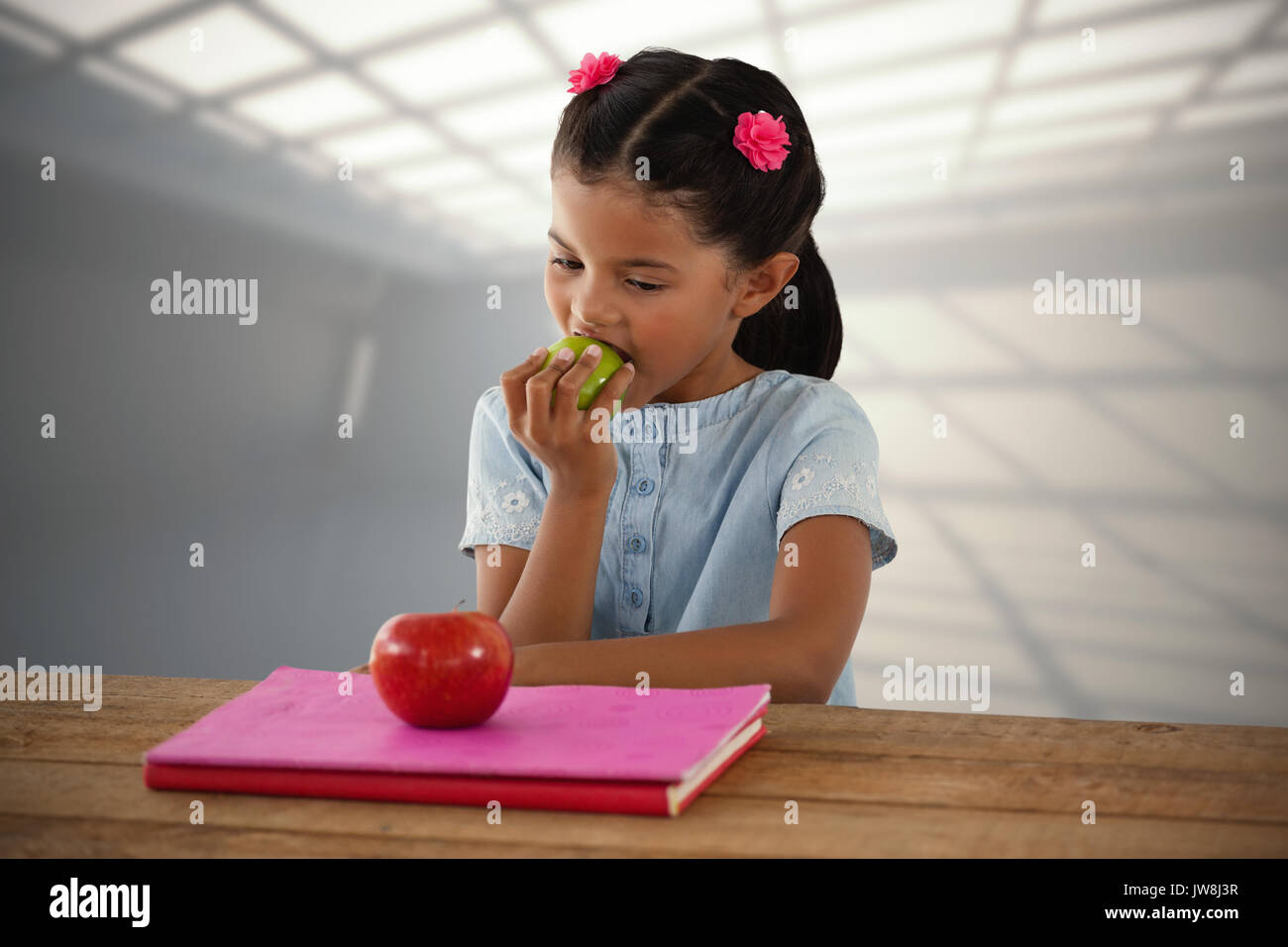 Girl eating Granny Smith apple at table against white room with windows at ceiling Stock Photo