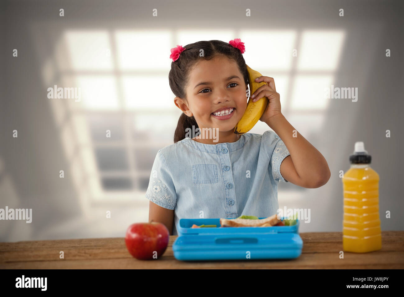 Smiling girl using banana as phone against room with large window showing city Stock Photo