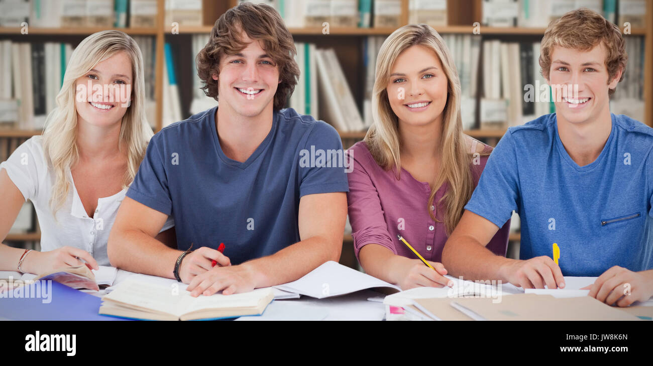 Four students looking at the camera against various multi colored books on shelf Stock Photo