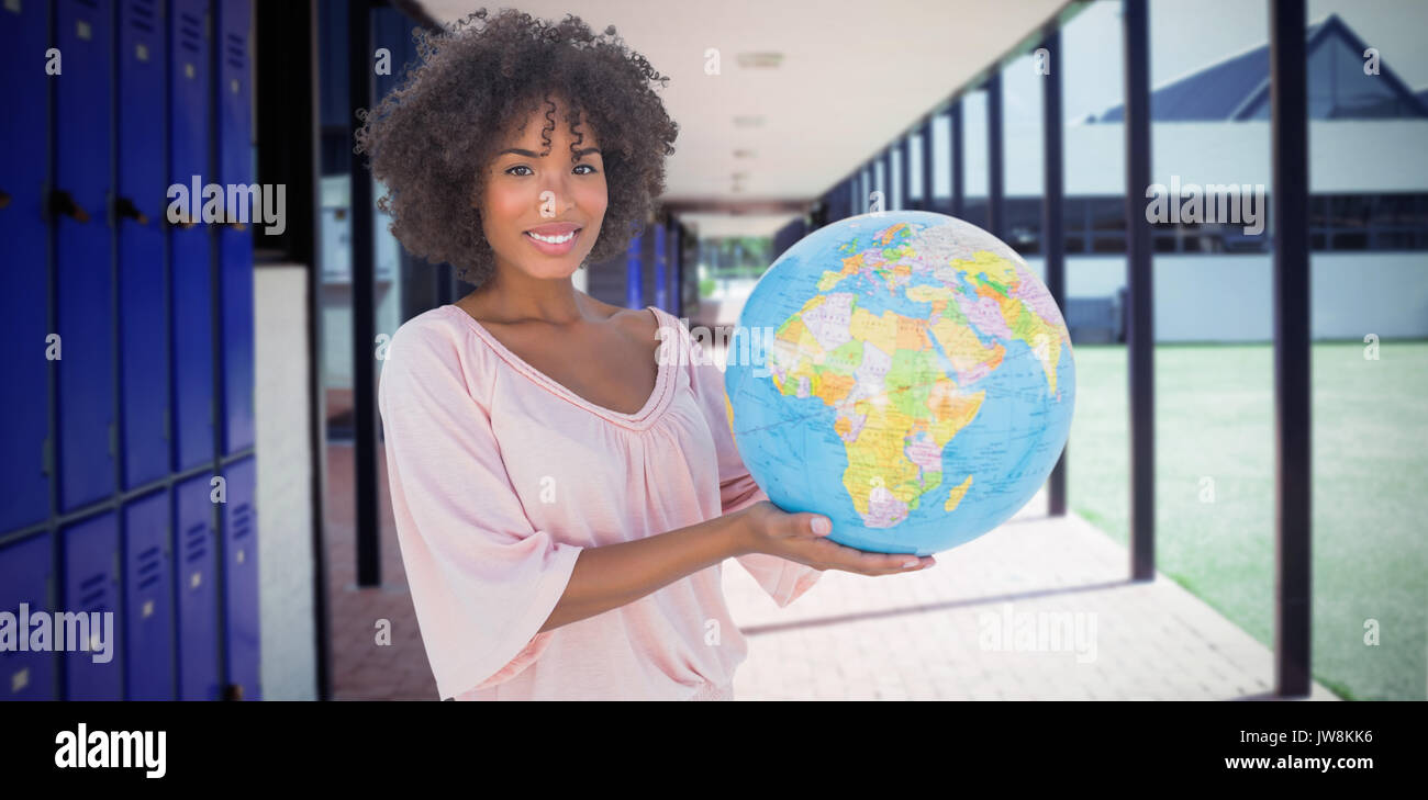 Smiling woman holding globe against empty corridor at school Stock Photo