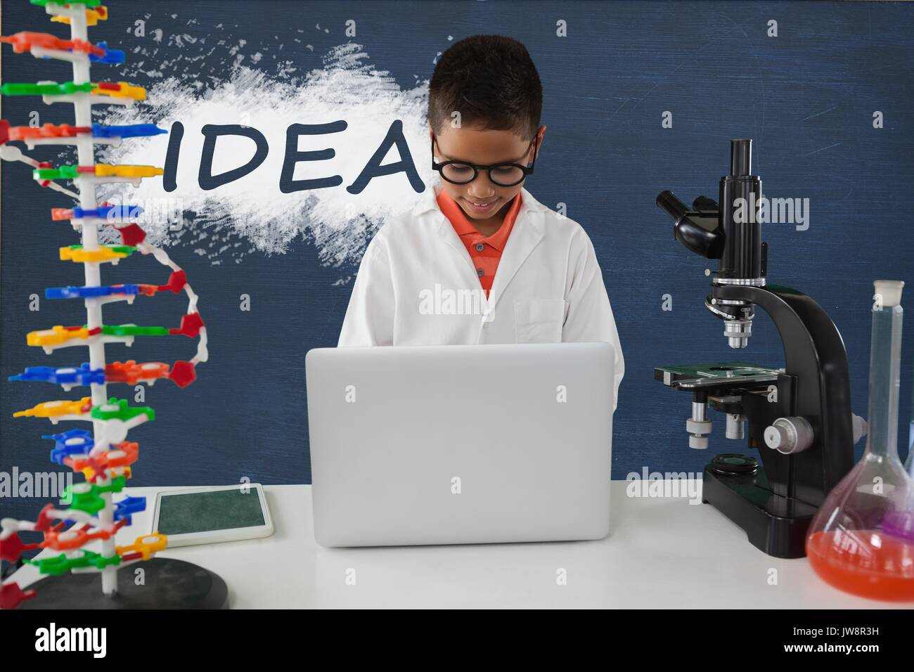 Digital composite of Student boy at table using a computer against blue blackboard with idea text Stock Photo